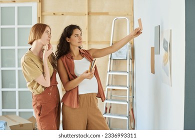 Young pregnant woman showing color swatch to her girlfriend while both choosing paint for walls of living room during renovation of apartment - Powered by Shutterstock