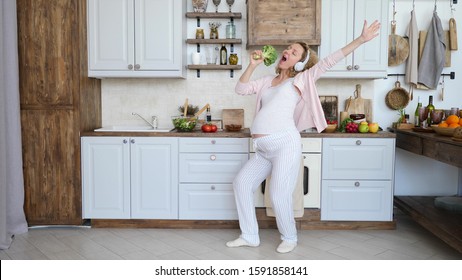 Young Pregnant Woman Singing In Broccoli Wearing Headphones Dancing In Kitchen.