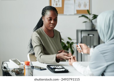 Young pregnant woman sitting in front of clinician checking her glucose level with digital medical device during consultation - Powered by Shutterstock