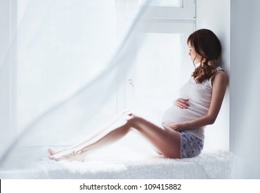 young pregnant woman sitting on the window