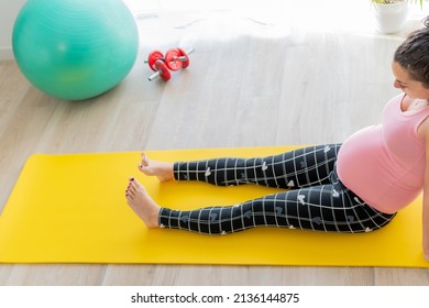 Young Pregnant Woman Sitting On The Floor On An Exercise Mat Does Exercises With Her Legs And Feet To Avoid Swollen Legs And Feet In Pregnancy. Body Care And Exercise In Pregnancy