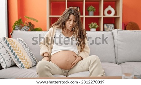 Young pregnant woman sitting on sofa breaking water at home