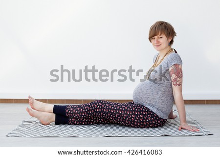 Young pregnant woman is sitting on the blanket on the floor, looking into the camera
