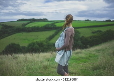 A young pregnant woman is standing in the countryside holding her baby bump - Powered by Shutterstock