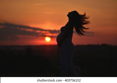 Young pregnant woman stands in the grass at sunset. Pregnant woman in dress standing in the sunset. Silhouette of a pregnant woman on the sky background
Silhouette of a pregnant woman at sunset