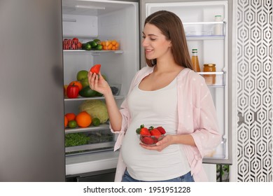 Young pregnant woman with strawberries near fridge at home. Healthy eating