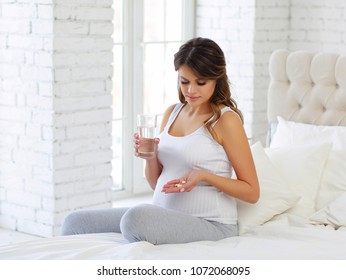 a young pregnant woman is taking medications and drinking water.