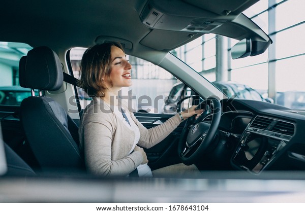 Young\
pregnant woman testing a car in car\
showroom