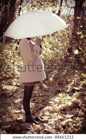 Young pregnant woman under umbrella in autumn forest