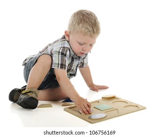 A young preschooler on the floor working on a wooden shape puzzle. On a white background.