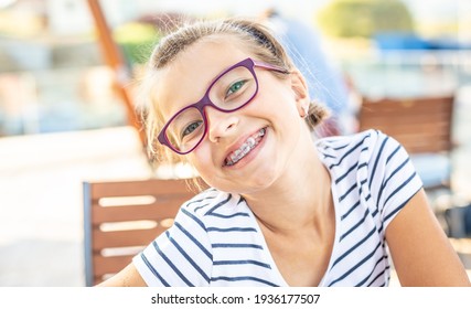 Young preteen girl in glasses wearing braces smiles at the camera on a summer day.