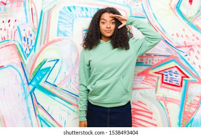 Young Pretty African American Woman Greeting The Camera With A Military Salute In An Act Of Honor And Patriotism, Showing Respect Against Graffiti Wall