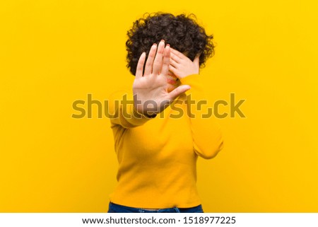 young pretty afro woman covering face with hand and putting other hand up front to stop camera, refusing photos or pictures