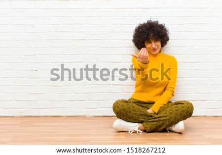 young pretty afro woman feeling happy, successful and confident, facing a challenge and saying bring it on! or welcoming you sitting on the floor