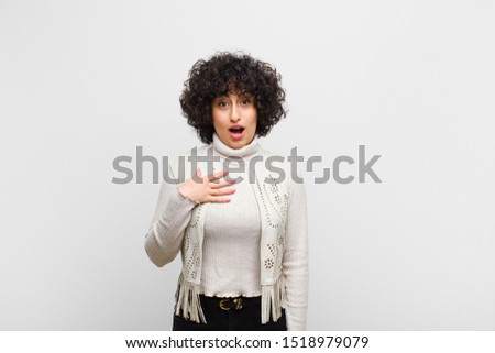 young pretty afro woman feeling shocked, astonished and surprised, with hand on chest and open mouth, saying who, me