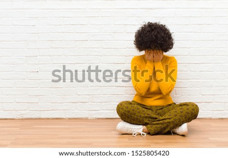 young pretty afro woman feeling sad, frustrated, nervous and depressed, covering face with both hands, crying sitting on the floor