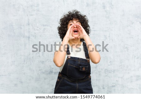 young pretty afro woman feeling happy, excited and positive, giving a big shout out with hands next to mouth, calling out