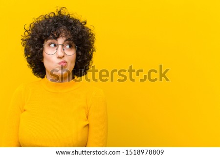 young pretty afro woman looking puzzled and confused, wondering or trying to solve a problem or thinking