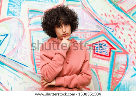 young pretty afro woman looking serious, confused, uncertain and thoughtful, doubting among options or choices against graffiti wall