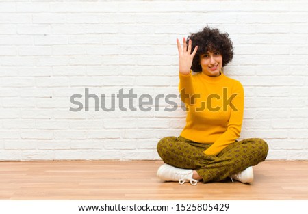 young pretty afro woman smiling and looking friendly, showing number four or fourth with hand forward, counting down sitting on the floor