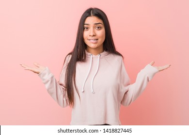 Young pretty arab woman wearing a casual sport look confused and doubtful shrugging shoulders to hold a copy space.