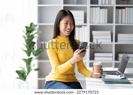 Young pretty Asian businesswoman using smartphone in the office room, contacting with customer.