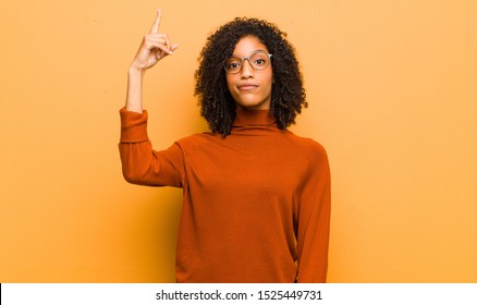 Young Pretty Black Woman Feeling Like A Genius Holding Finger Proudly Up In The Air After Realizing A Great Idea, Saying Eureka Against Orange Wall