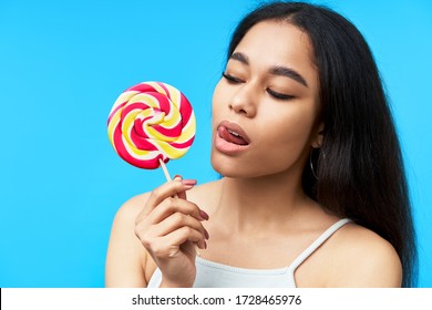 Young Pretty Black Woman Licking Colorful Lollipop On Blue Background. Desire Concept 