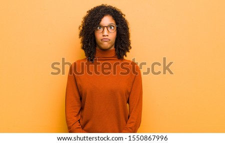 young pretty black woman looking goofy and funny with a silly cross-eyed expression, joking and fooling around against orange wall