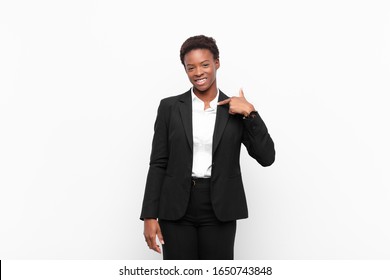 young pretty black womanlooking happy, proud and surprised, cheerfully pointing to self, feeling confident and lofty against white wall