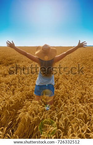 Young pretty blond girl happy looking at the sun in the zenith. She is wearing a hat. Transmission field. Back view.