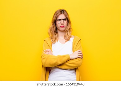 young pretty blonde woman feeling displeased and disappointed, looking serious, annoyed and angry with crossed arms against yellow wall