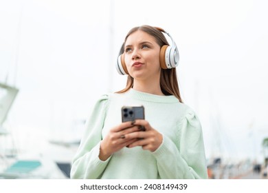 Young pretty blonde woman listening music with a mobile and thinking - Powered by Shutterstock