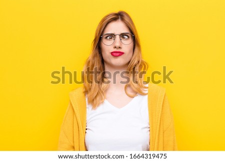 young pretty blonde woman looking goofy and funny with a silly cross-eyed expression, joking and fooling around against yellow wall