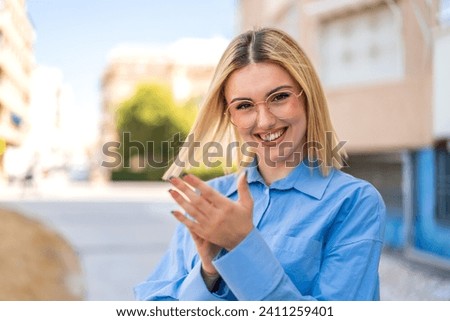 Young pretty blonde woman at outdoors With glasses and applauding