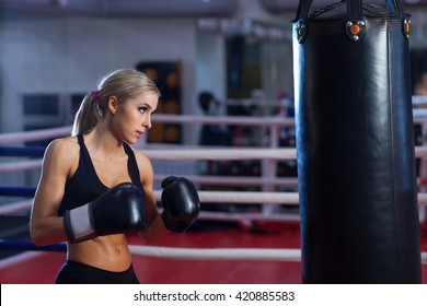 Young pretty boxer woman standing on ring and doing exercise with punching bag