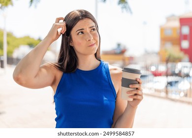 Young pretty Brazilian woman holding a take away coffee at outdoors having doubts and with confuse face expression - Powered by Shutterstock