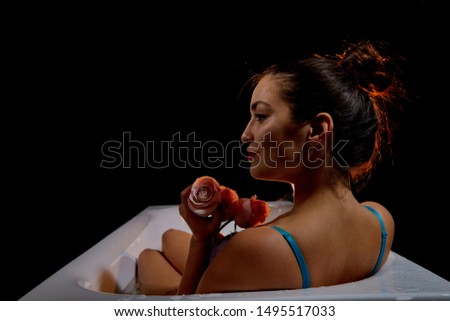 Young pretty brunette woman in bath with water and flowers. Model during an unusual photo shoot in a dark room