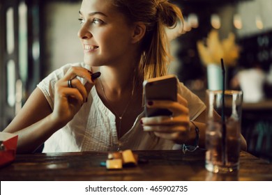 young pretty brunette woman eat chocolate in cafe, using smartphone, touch screen display, sweet food, tasty breakfast, close up portrait, hipster girl, fanny  - Powered by Shutterstock