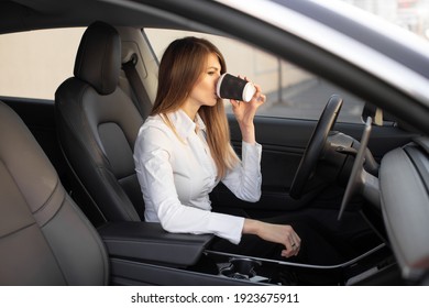 Young Pretty Businesswoman Drinking Take Away Coffee, Sitting Inside Of Autonomous Driverless Electric Car. Self-driving Vehicle. Automotive Technology.