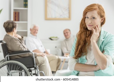 Young Pretty Carer In Nursing Home And Patients Behind Her