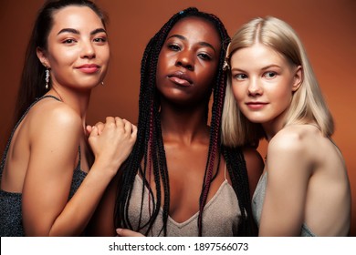 young pretty caucasian, afro, asian woman posing cheerful together on brown background, lifestyle diverse nationality people concept