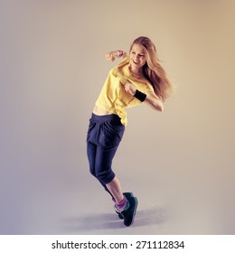 Young pretty Caucasian hip hop girl dancing with fun. Active fitness trainer posing in studio. 
