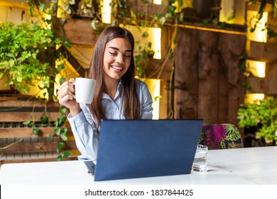 Young pretty caucasian woman in cafe in city centre with tablet laptop, studying on laptop and enjoying coffee
