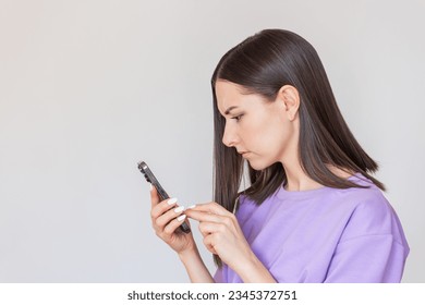young pretty Caucasian woman in a purple T-shirt is excited and holding in her hand.She received an unpleasant message,frowns, worries and anxiously writes reply message.isolated on a light background - Shutterstock ID 2345372751