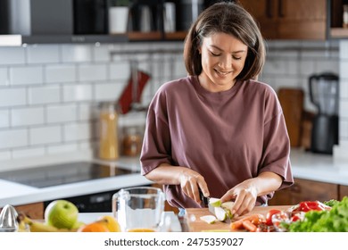 A young pretty cheerful woman is preparing a healthy various vegetable-based meal at home - Powered by Shutterstock