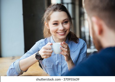 Young pretty cheerful woman sitting and drinking coffee in cafe with bearded man 