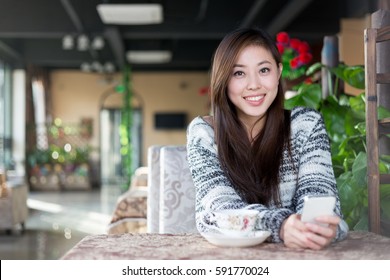 Young Pretty Chinese Woman Sitting In Modern Cafe