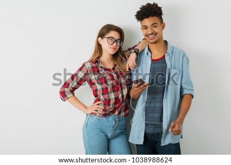 young pretty couple, handsome black man, beautiful girl, glasses, isolated, youth, hipster style, students, friends together, smiling happy, holding smartphone, listening to music on earphones