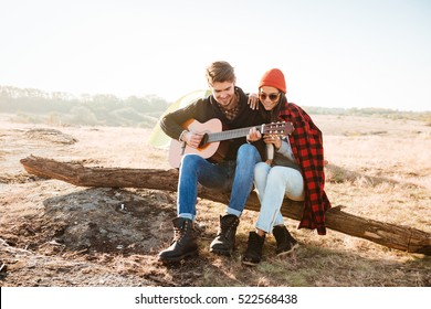 Young pretty couple having fun outdoors with guitar while sitting at the campsite - Powered by Shutterstock